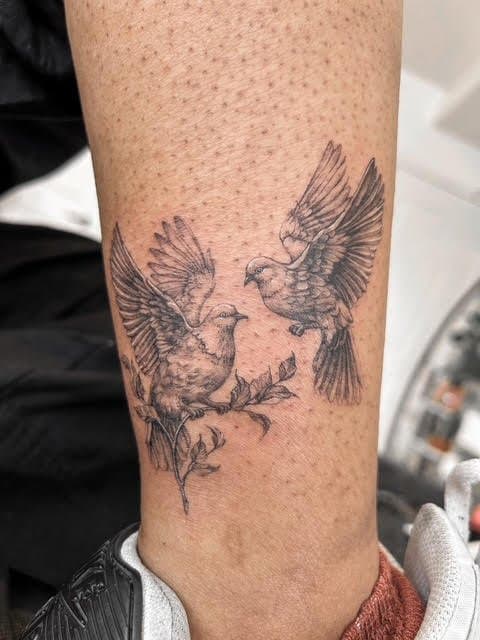 Tattoo of two birds in flight on a person's leg.