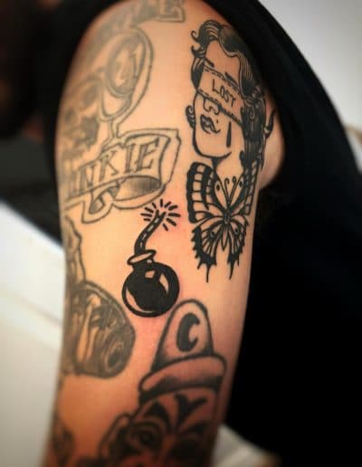 Tattooed arm with bomb, blindfolded woman, and butterfly designs
