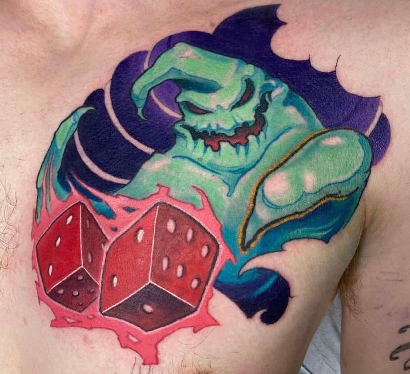 Colorful tattoo of a green, menacing-looking creature with sharp claws, surrounded by dark purple and teal elements, with red dice in the foreground.