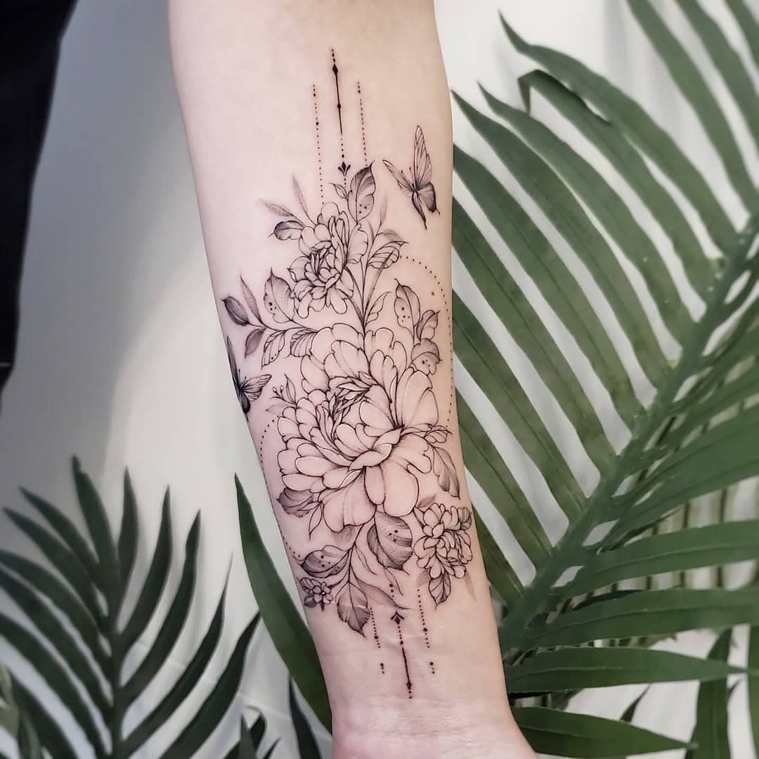 Fine-line forearm tattoo with layered flowers, leaves, dotted ornaments, and butterflies