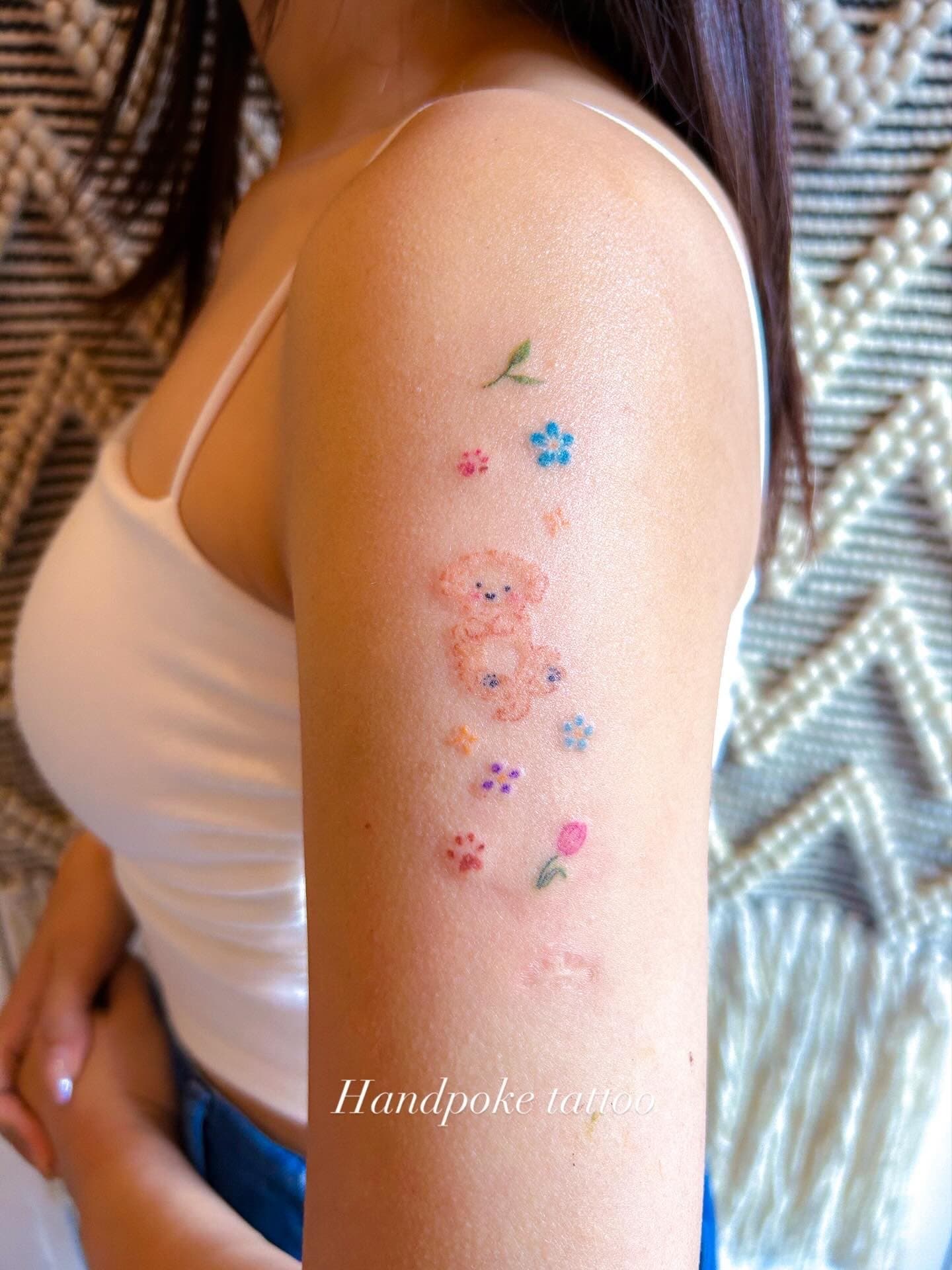 Hand-poked tiny coloured flowers and two small teddy bears on the upper arm