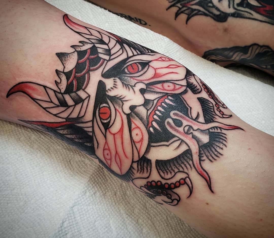 Tattoo of a dragon with red and black ink on a person's arm.
