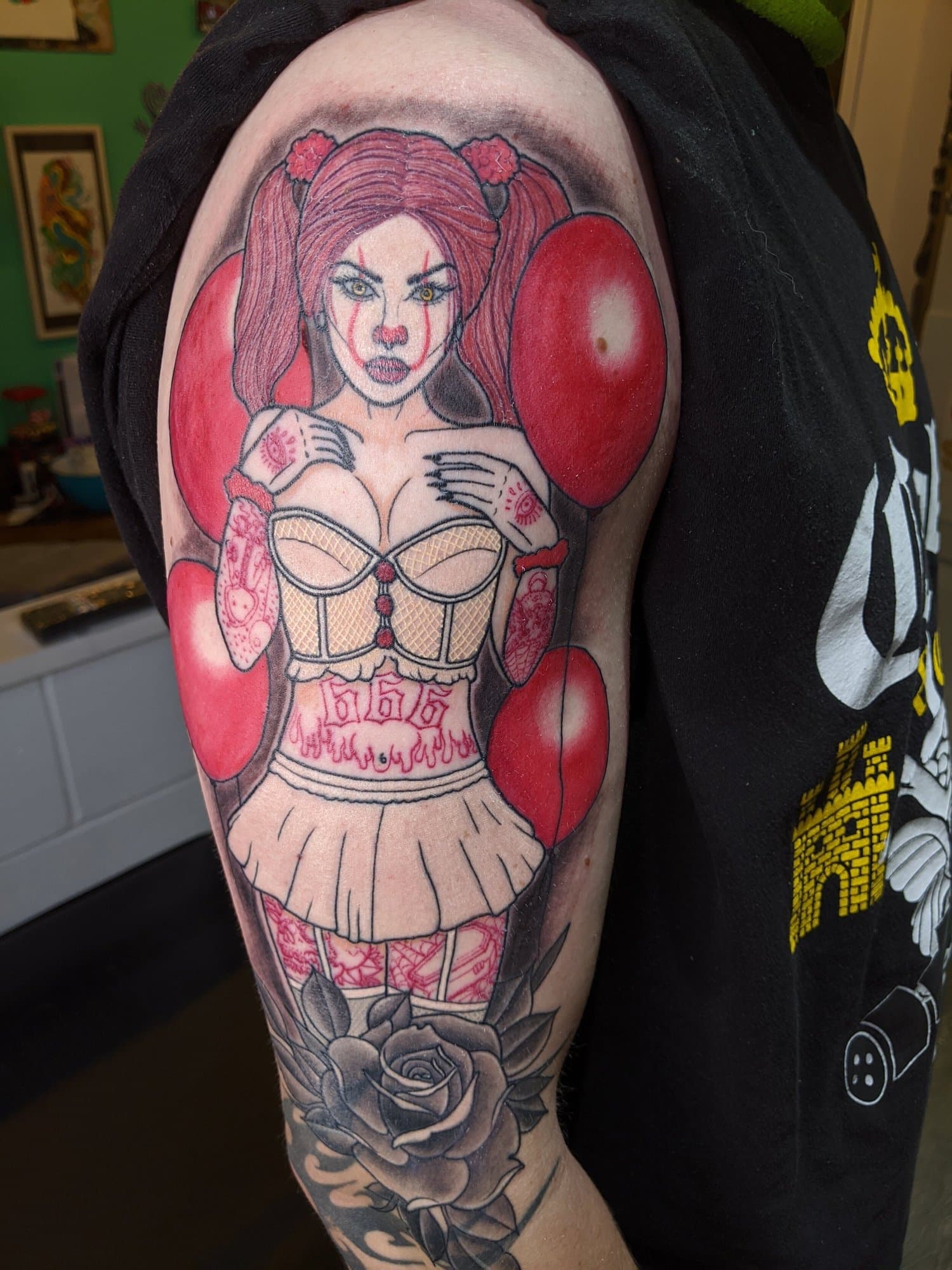 Colour tattoo inspired by IT of a red-haired female clown surrounded by red balloons, with decorative clothing and a black and grey rose below.