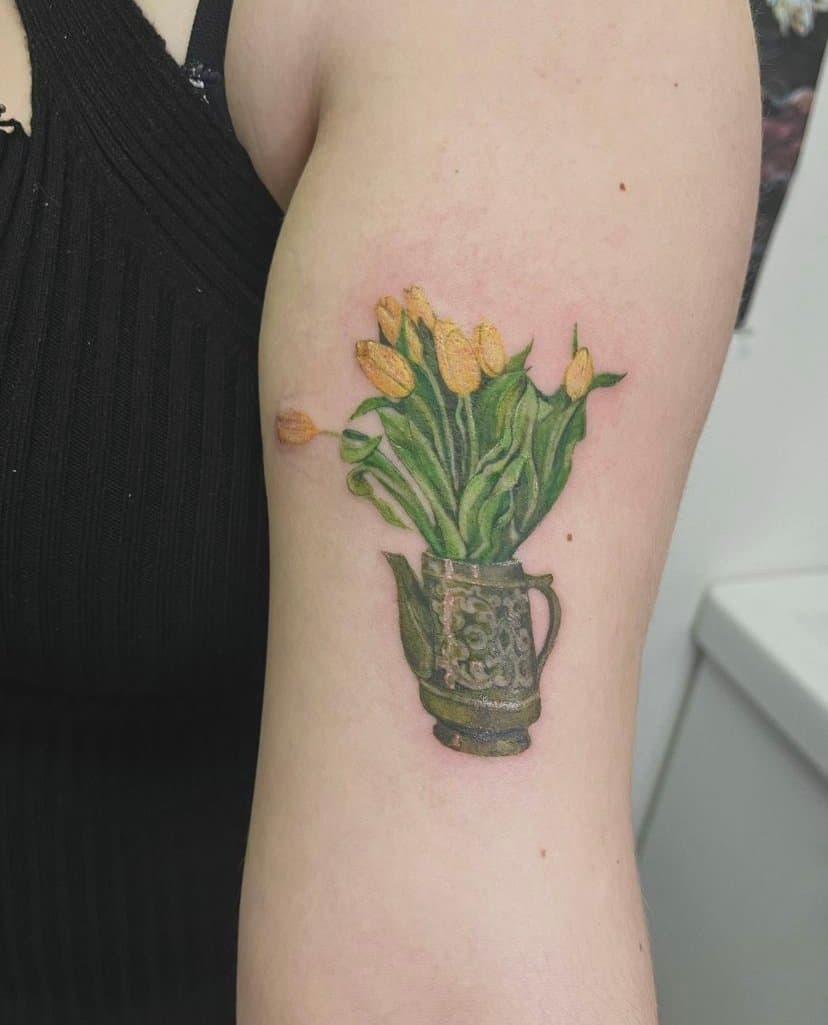 Tattoo of a yellow tulip bouquet in a decorative dark ceramic vase on person's upper arm.