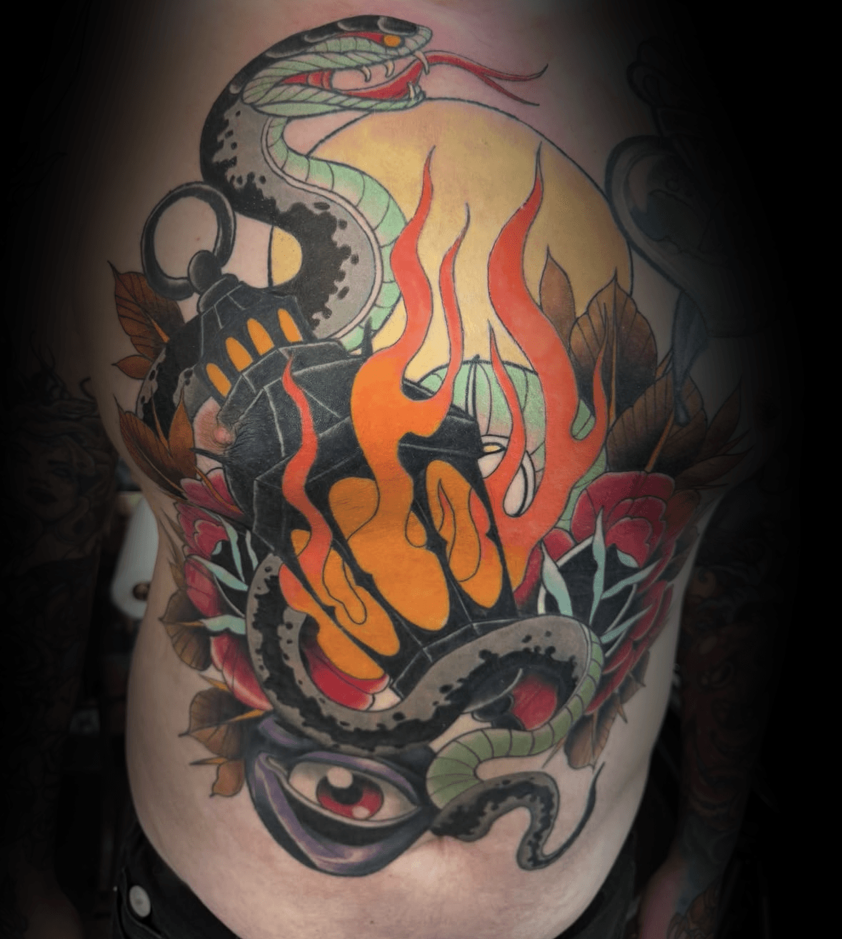 Colorful tattoo on a person's arm featuring a snake, flames, flowers, an eye and mechanical elements by Rob Adams, tattoo artist at Sundog Studios in Airdrie Al