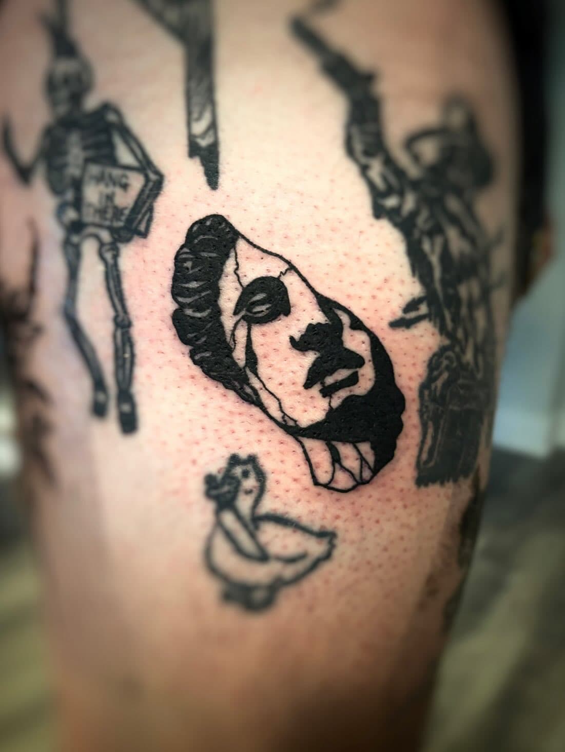 Close-up of a black ink tattoo of a skull mask and a duck