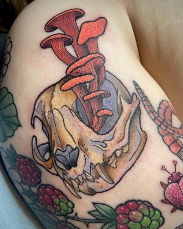 Tattoo of a skull with mushrooms and forest elements on skin.