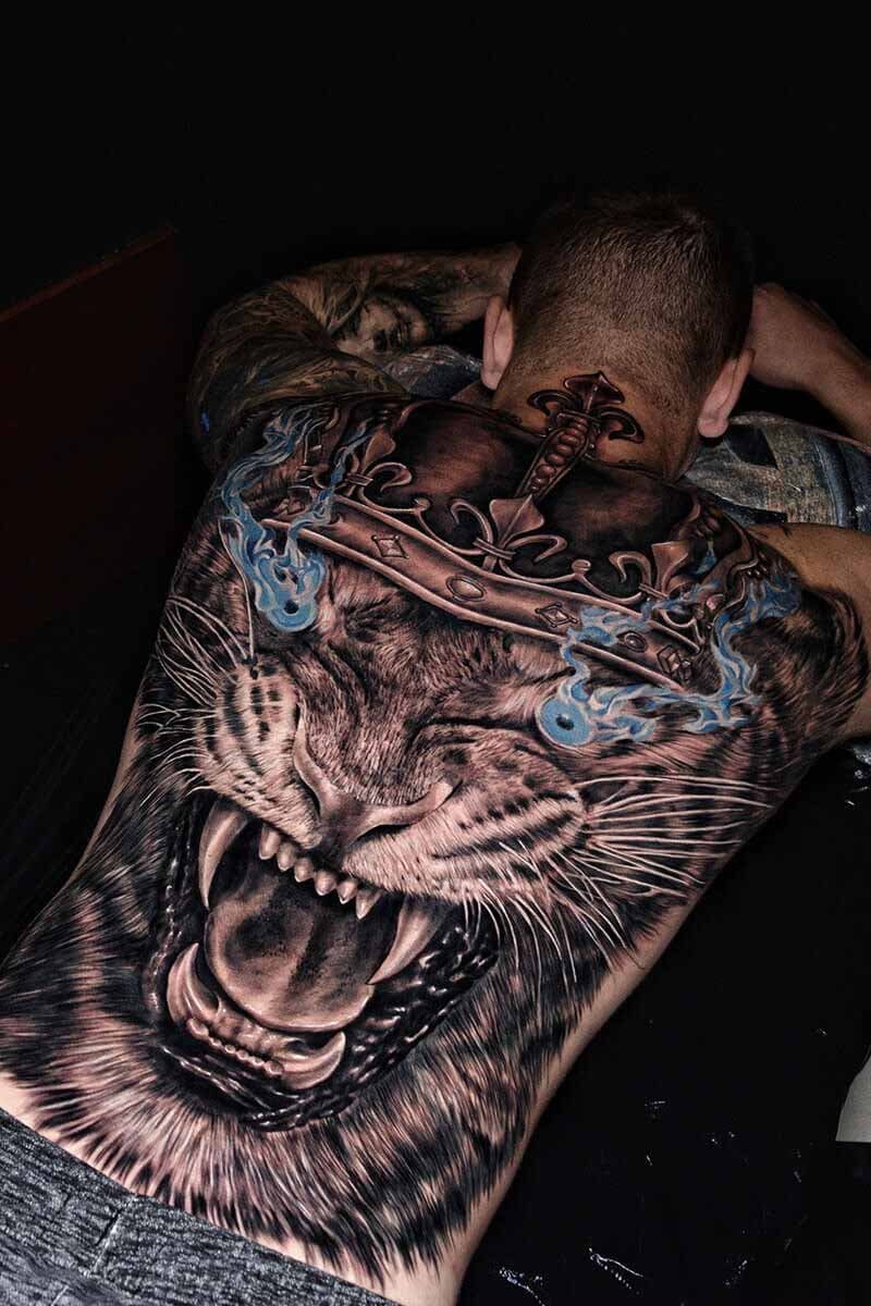 Atticus Tattoo| Black and grey realism tattoo of a lion, wearing a crown and blue flames coming out of its eyes