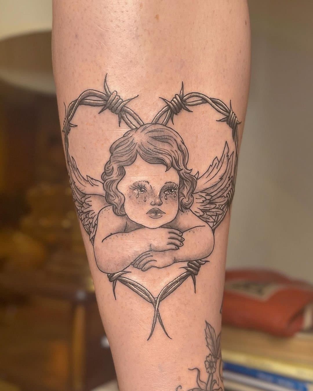 Illustrative forearm tattoo of a cherub inside a barbed-wire heart
