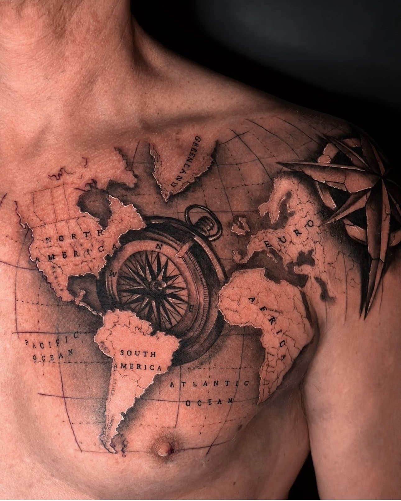 Tattoo of vintage world map and compass on a person's chest.