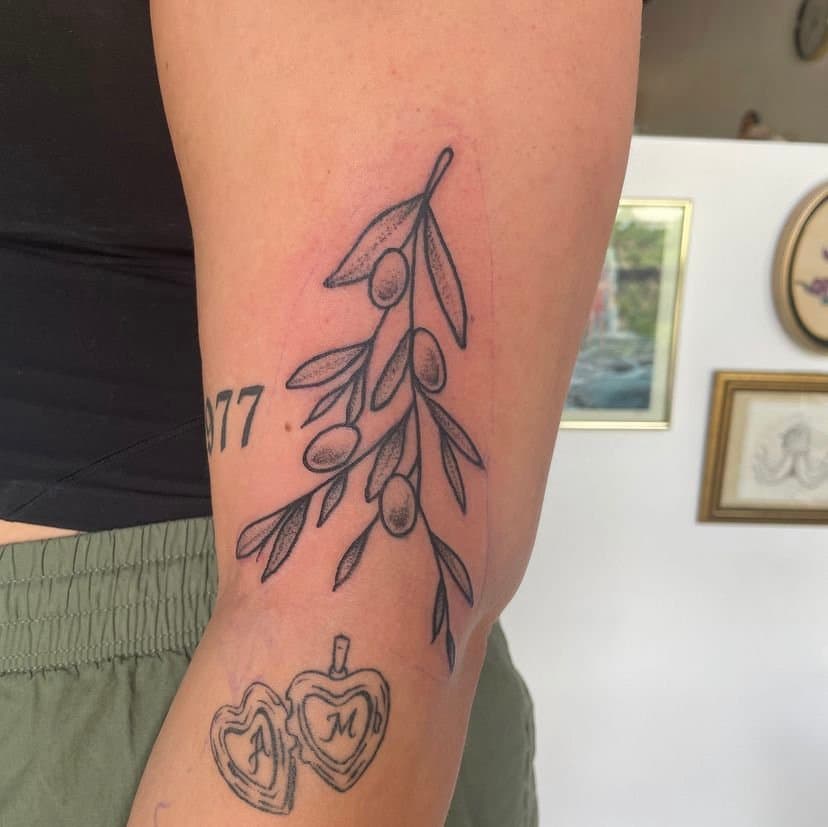 Tattoo of olive branch with olives and a separate tattoo of two hearts with initials 'A' and 'M' inside them.