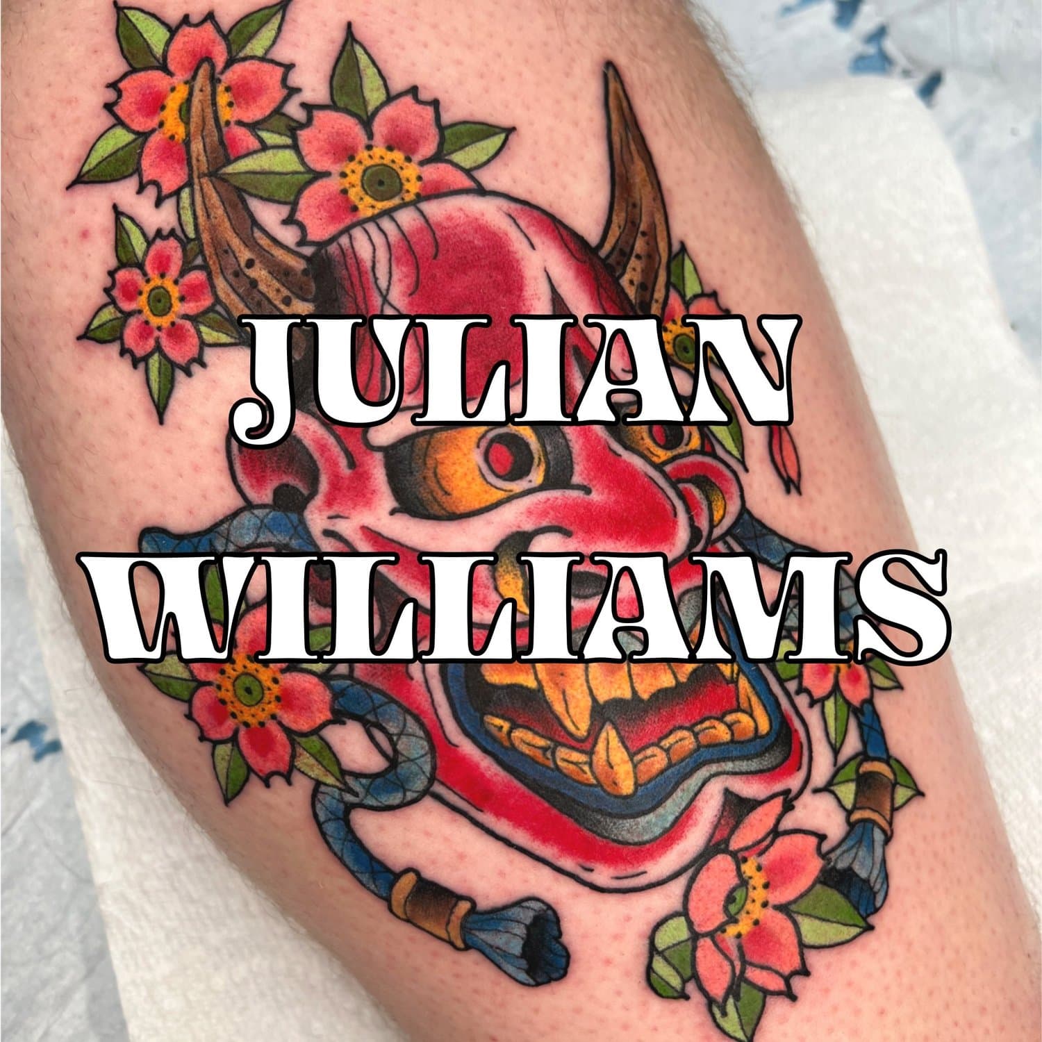 Tattoo by Julian Williams of a red Hannya mask with pink cherry blossoms.