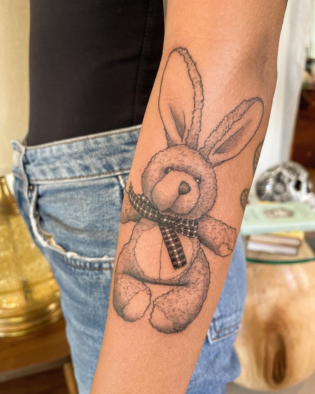 Illustrative forearm tattoo of a stuffed rabbit with a ribbon