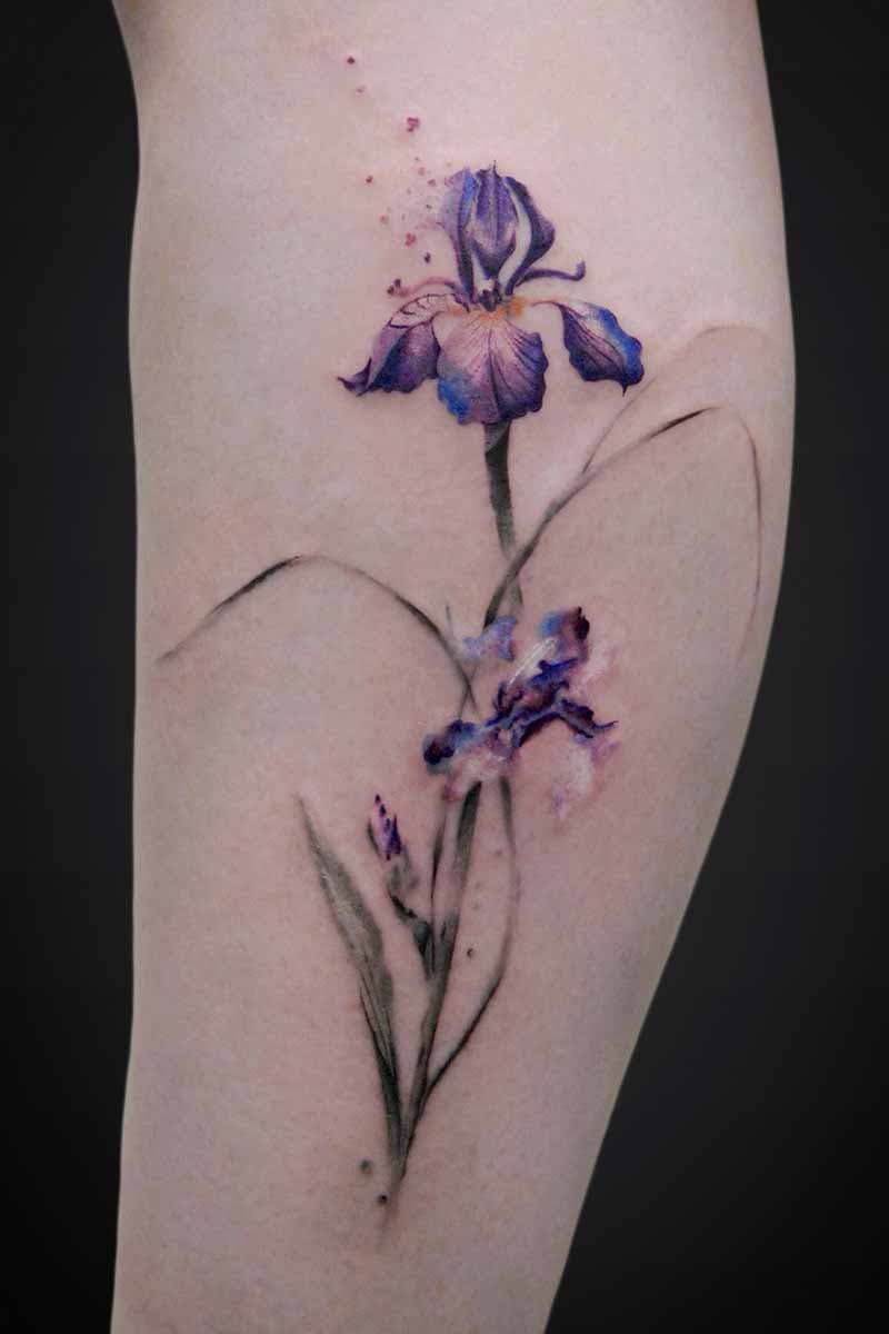Watercolor-style purple iris tattoo along the back of a leg with delicate green stems and leaves.