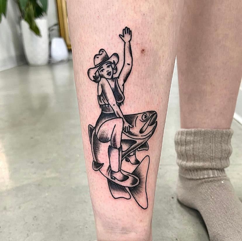 Tattoo of a cartoon girl wearing a hat, sitting on a fish, raising her hand, with fish bubbles around her.