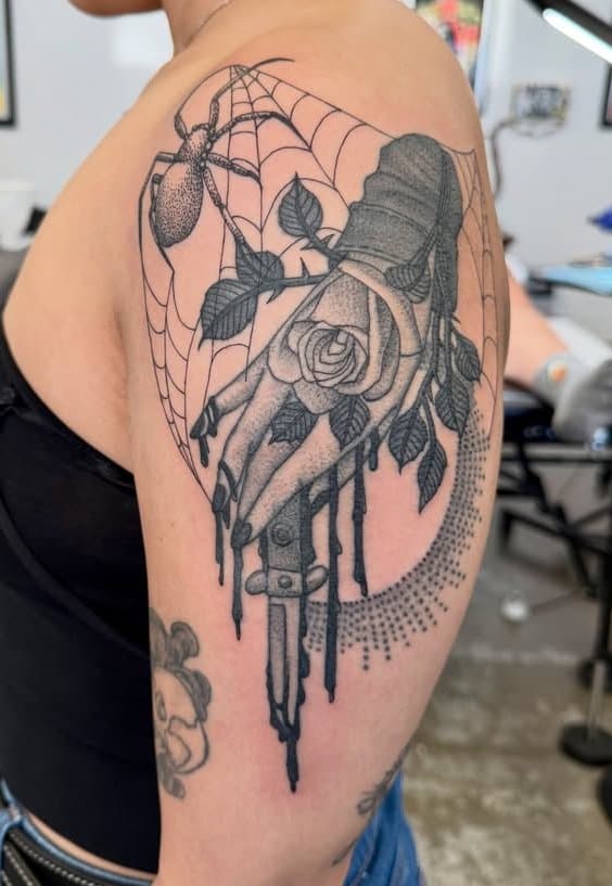 Dotwork hand holding a rose with a spider and web tattooed on a shoulder