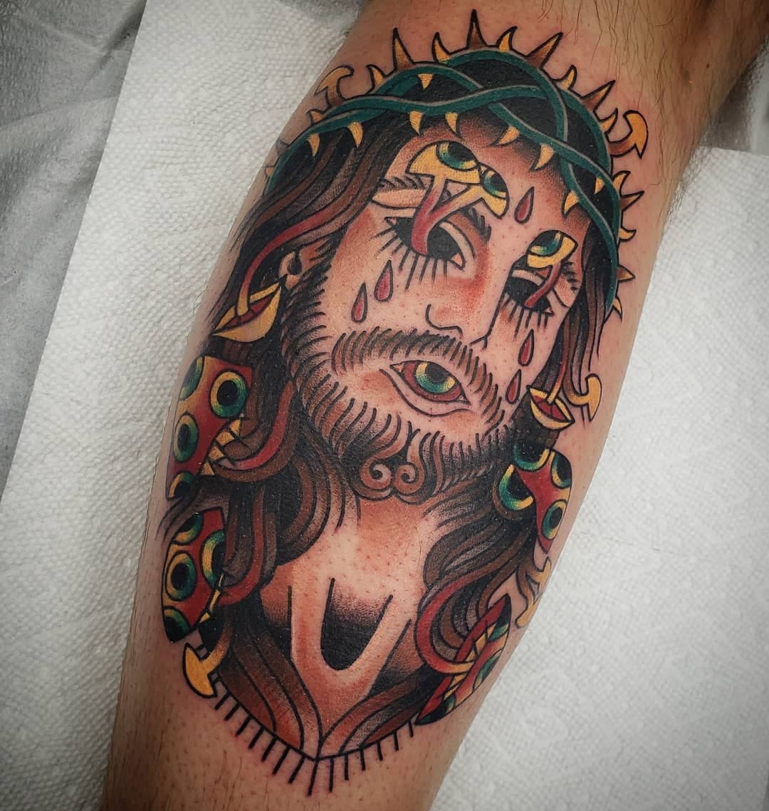 Tattoo of Jesus Christ with a crown of thorns, tears on his face, and a detailed beard and hair, on a person's arm.