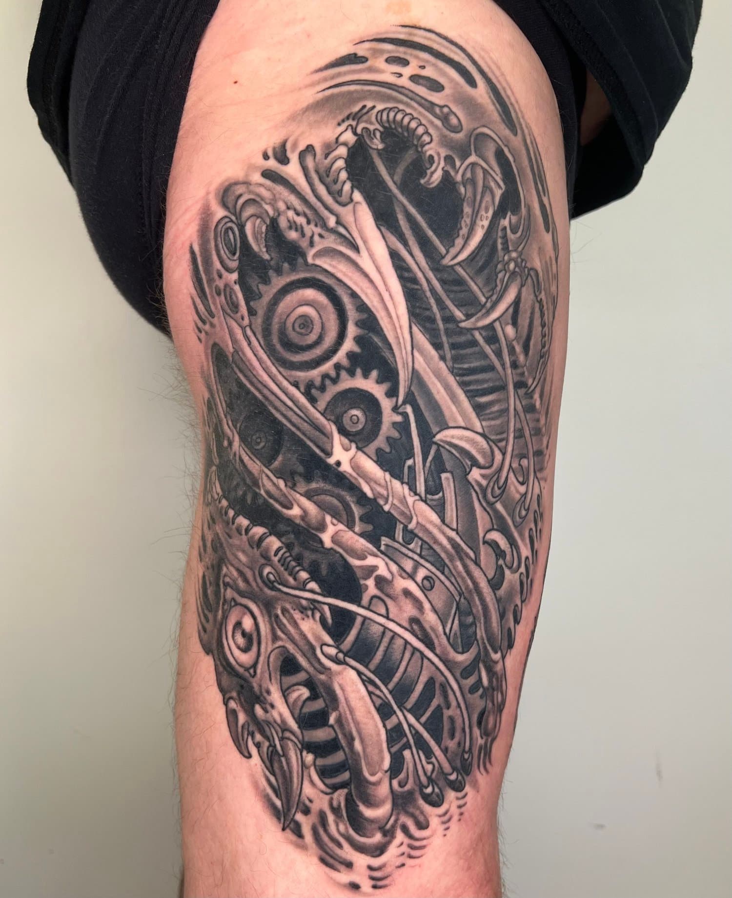 Black-and-grey biomechanical tattoo covering a thigh