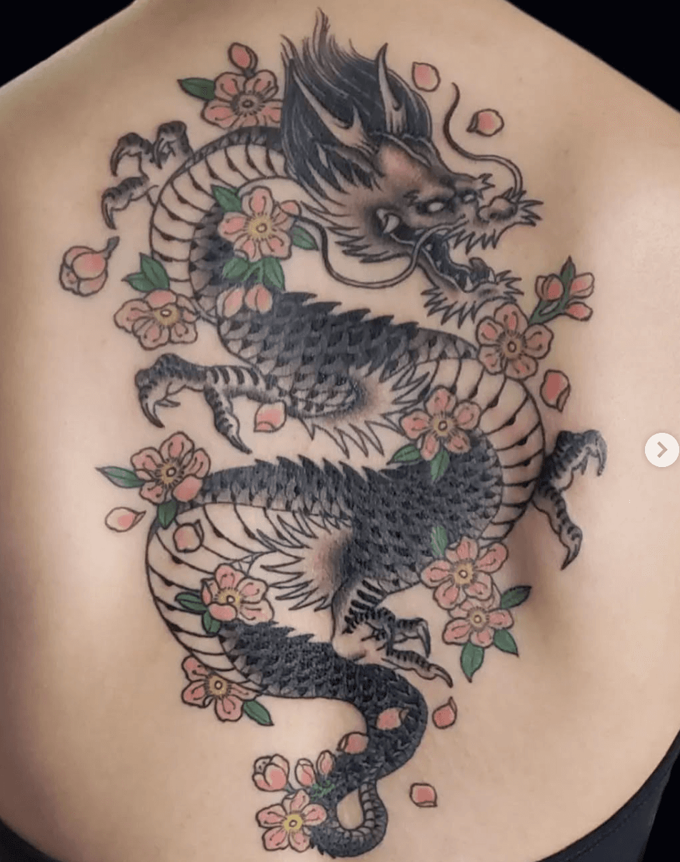 Tattoo of a traditional Japanese dragon surrounded by pink cherry blossoms on skin.