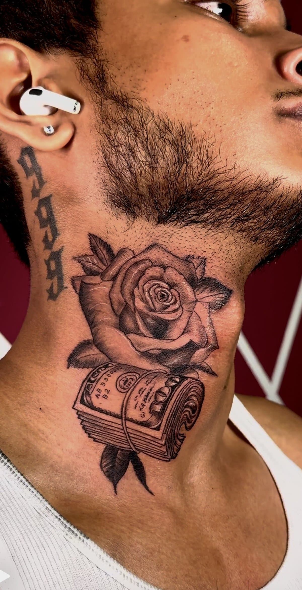 Man's neck shows a tattoo of a rose above a roll of cash, with '999' tattooed behind the ear.