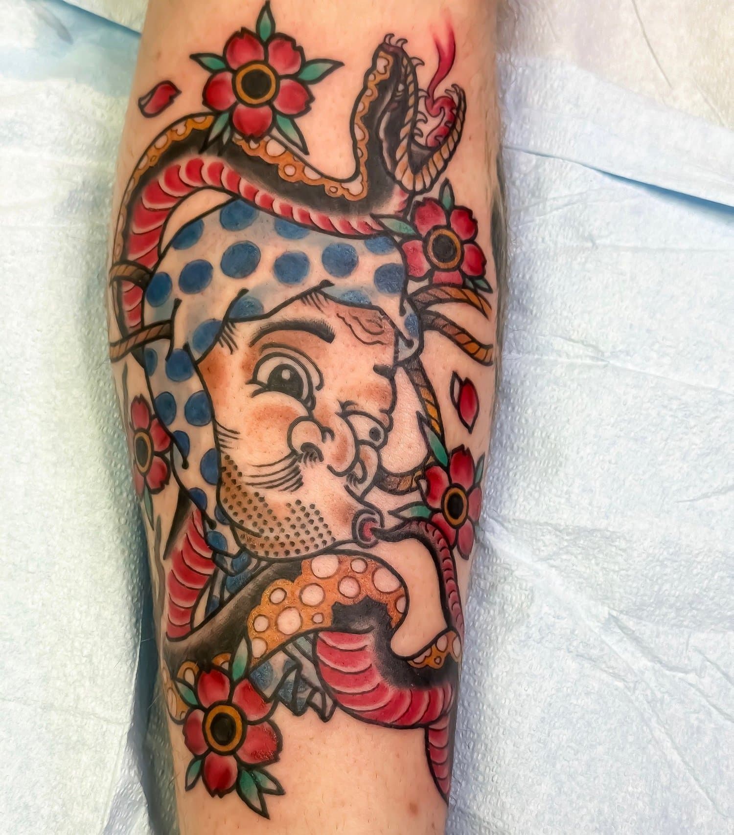 A tattoo of a traditional style pin-up girl with flowers and a snake on her head and body.