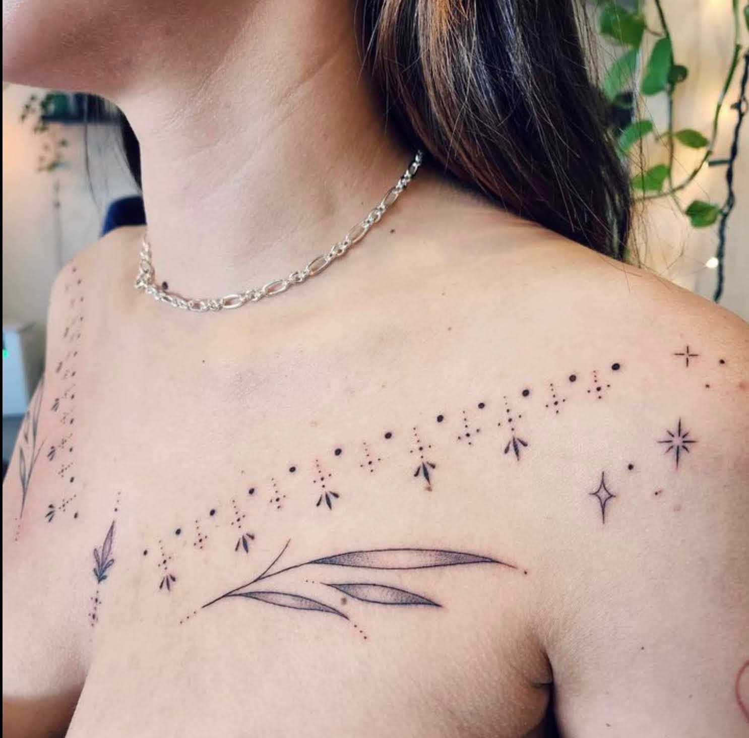 Symmetrical fine-line and dotwork collarbone ornament with leaves, stars, and small geometric marks
