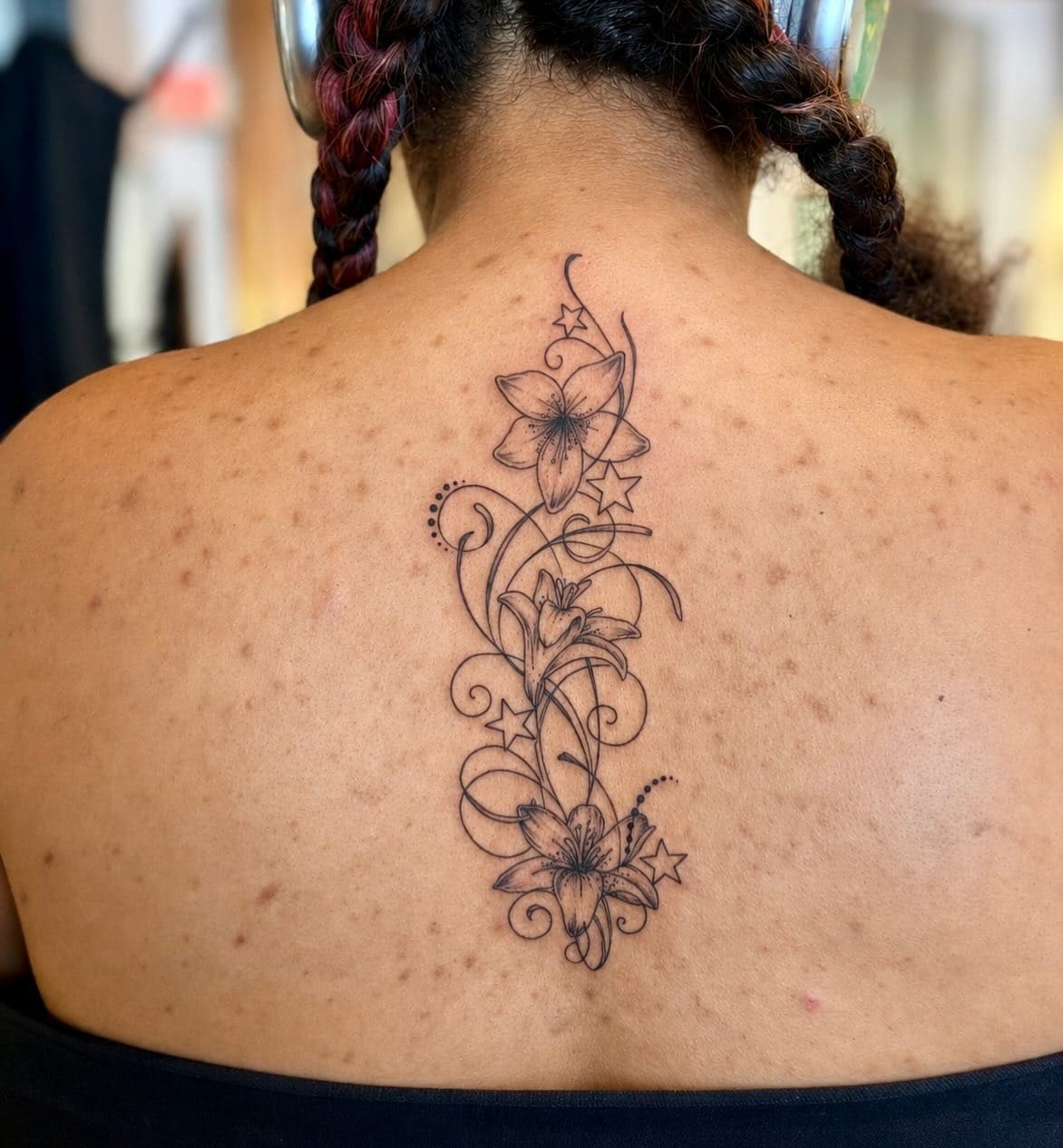 Close-up of a black ink floral tattoo with stars on a woman's upper back
