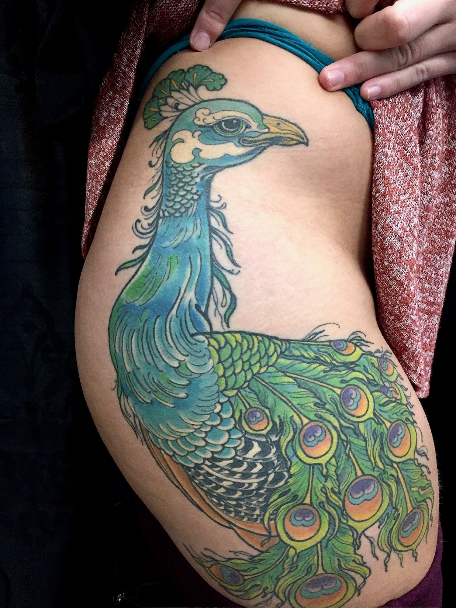 Colorful tattoo of a peacock on a person's thigh.