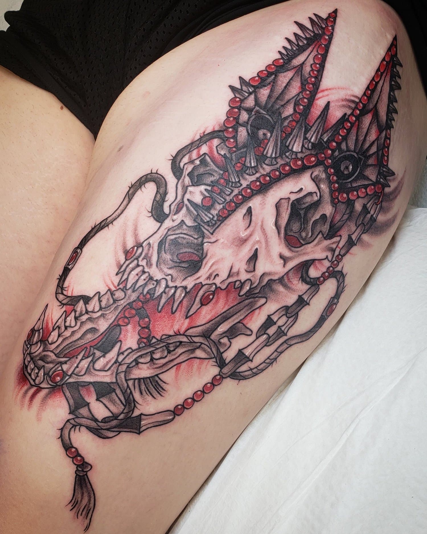 Tattoo of a skull wearing a demon-like crown with chains and beads.